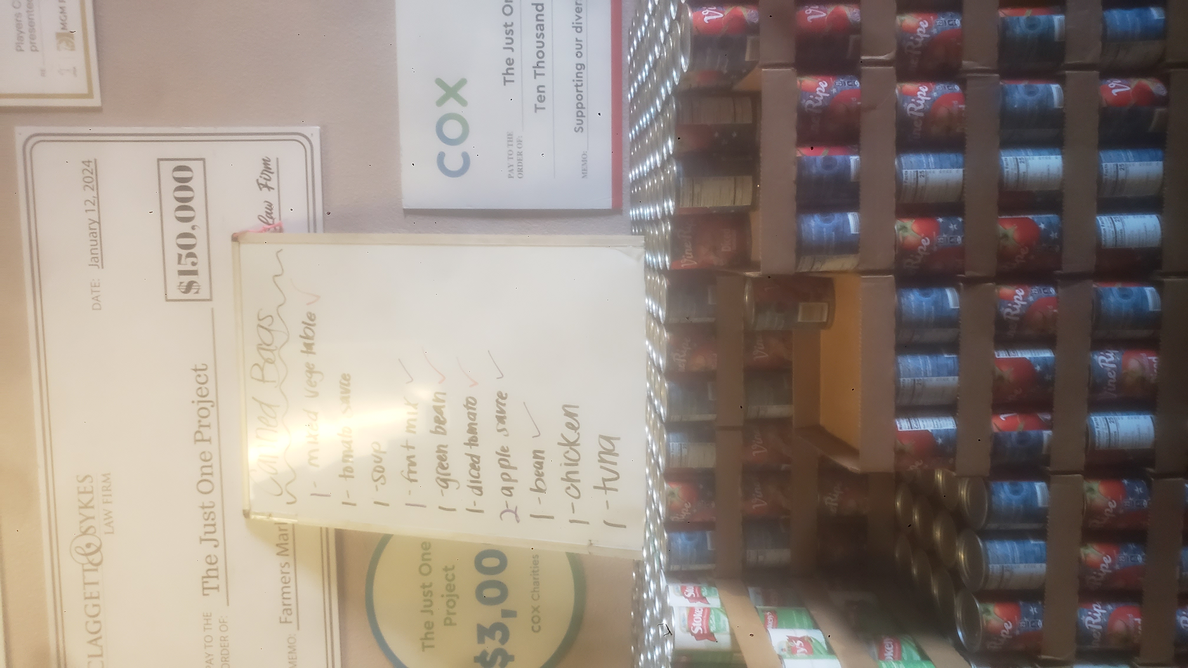 Stack of cans of diced tomatoes on trays with a dry erase board that has what goes in each bag written.